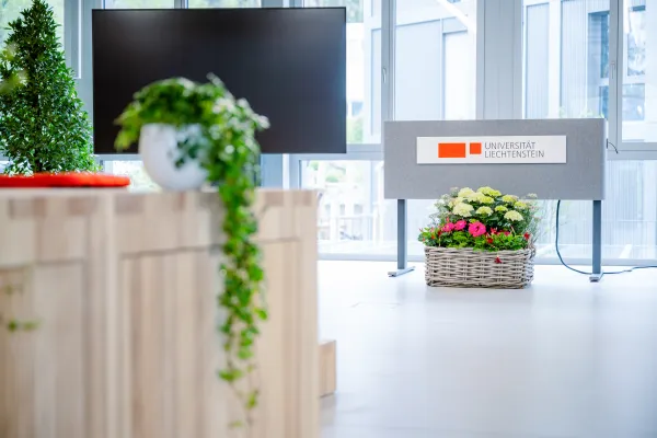 Rednerpult mit Logo der Universität Liechtenstein, umgeben von Pflanzen