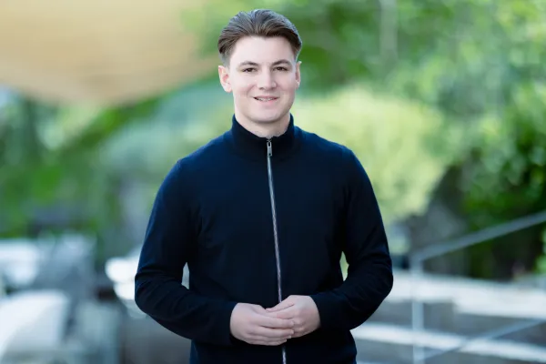 Student Bachelor BWL der Universität Liechtenstein im schwarzen Pullover lächelt in die Kamera – Campusaufnahme 