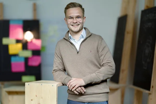 Student der Universität Liechtenstein im braunen lächelt in die Kamera – Campusaufnahme in freundlicher Lernumgebung.