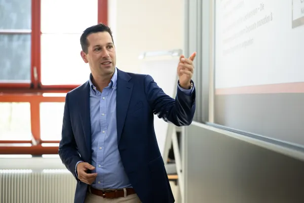 Nahaufnahme eines Dozenten, der auf eine Folie zeigt und einen Sachverhalt erklärt, im Unterricht an der Universität Liechtenstein.
