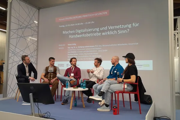 Podiumsdiskussion auf der Messe «Holz Handwerk 2024» in Nürnberg. Fünf Personen sitzen auf einer Bühne vor einer Leinwand mit dem Titel "Machen Digitalisierung und Vernetzung für Handwerksbetriebe wirklich Sinn?". Die Diskussion thematisiert die Rolle der Digitalisierung im Handwerk.