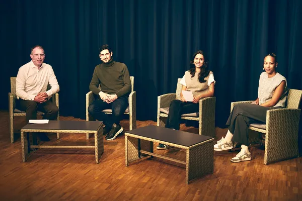 Vier Personen sitzen auf einer Bühne in Korbstühlen, vor einem dunklen Vorhang. Sie sind Teil einer Diskussionsrunde über Upcycling in der Architektur an der Universität Liechtenstein.