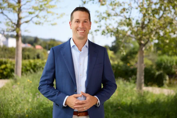 Porträt eines lächelnden Mannes im blauen Anzug im Freien an der Universität Liechtenstein.