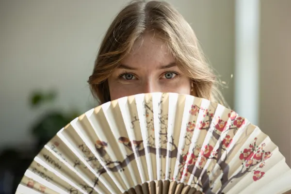 Junge Frau blickt über Fächer mit Blumenmuster in die Kamera.