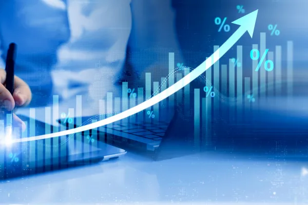 Person analysiert Wirtschaftsdaten an Laptop und Tablet mit steigender Kurve und Prozentzeichen.