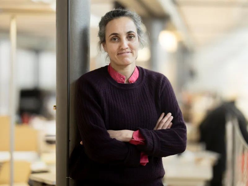 Porträt einer Frau mit schwarzem Pullover, die mit verschränkten Armen an einer Säule lehnt